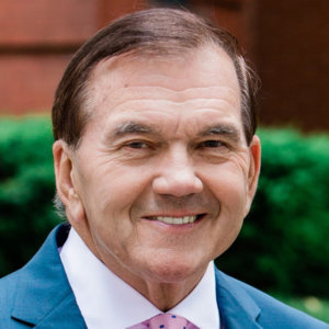 Governor Tom Ridge headshot wearing a blue suit and pink tie. Ridge is a white man who has short brown hair