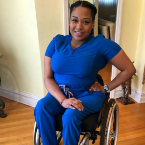 Andrea Dalzell wearing scrubs, smiling. Dalzell is a person of color who uses a wheelchair