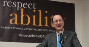 Brad Sherman speaking at the microphone with a RespectAbility banner behind him