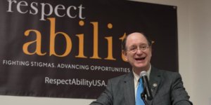 Brad Sherman speaking at the microphone with a RespectAbility banner behind him