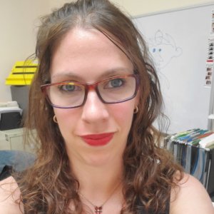 Carly Okyle headshot smiling. Okyle is white, has long brown hair and is wearing glasses.