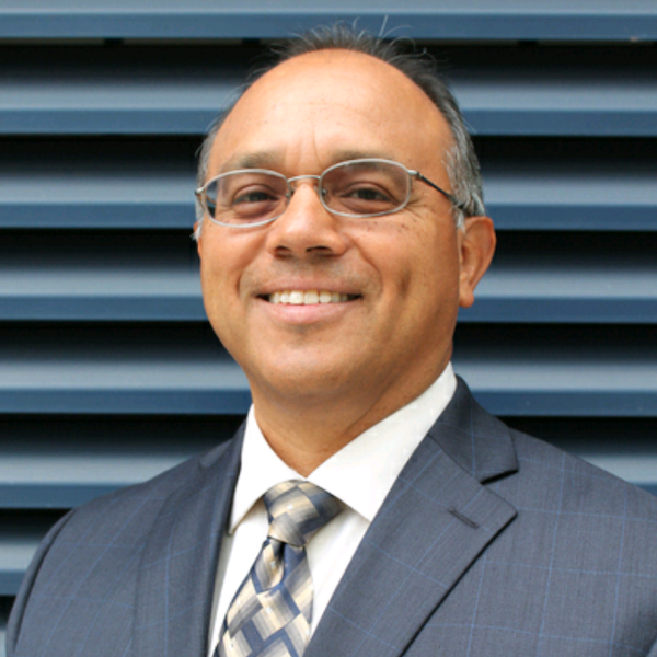 Jaime Pacheco Orozco smiling wearing a suit and tie and glasses. Jaime has short black hair