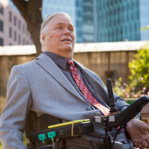 Lex Frieden smiling wearing a suit and tie. Frieden uses a power wheelchair.