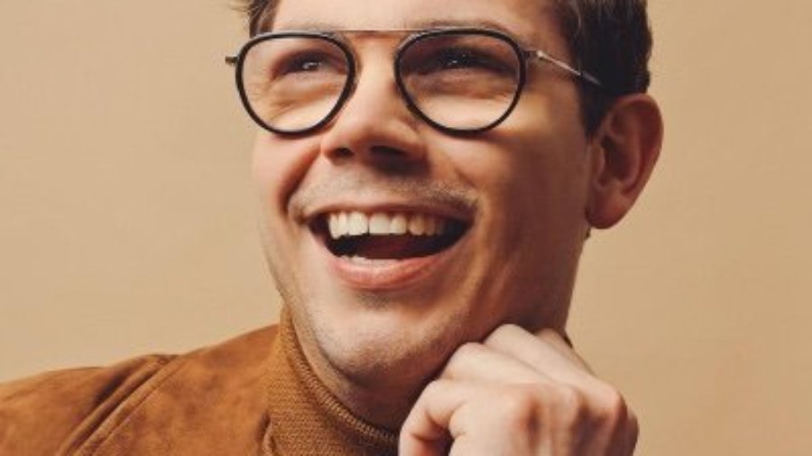 Ryan O'Connell smiling headshot wearing glasses and a brown jacket. Ryan is a white man with short brown hair
