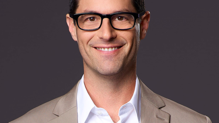 David Schulner smiling headshot. Schulner is a white man with short black hair, is wearing glasses and a tan suit