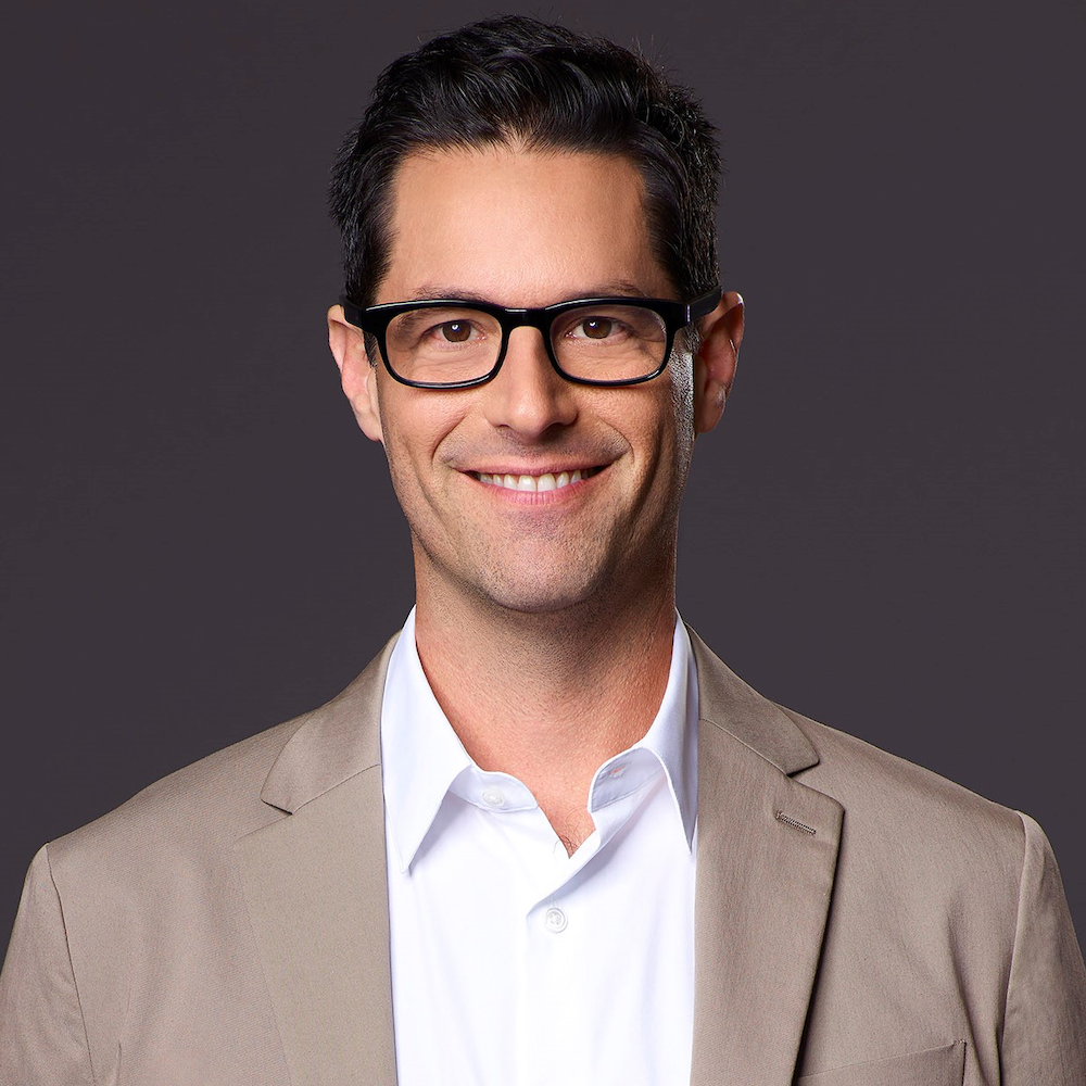 David Schulner smiling headshot. Schulner is a white man with short black hair, is wearing glasses and a tan suit
