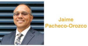 Jaime Pacheco Orozco smiling wearing a suit and tie and glasses. Jaime has short black hair. Text: Jaime Pacheco-Orozco