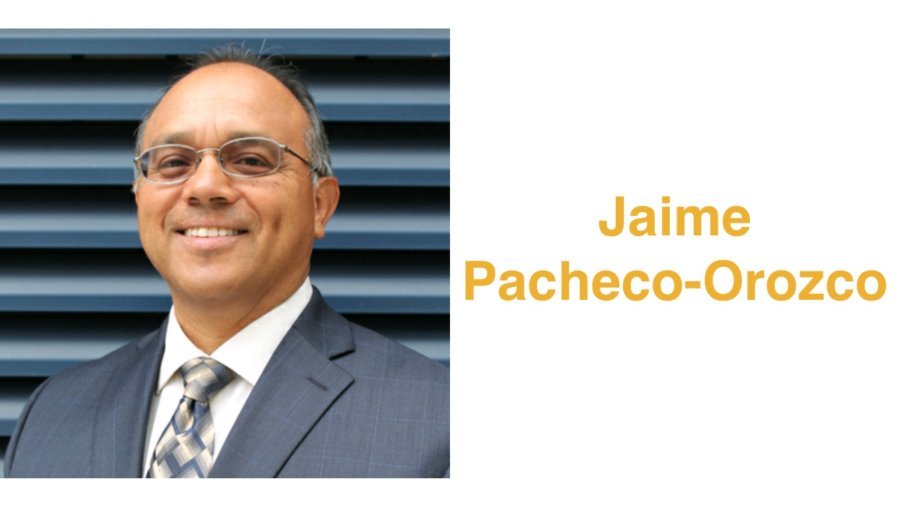 Jaime Pacheco Orozco smiling wearing a suit and tie and glasses. Jaime has short black hair. Text: Jaime Pacheco-Orozco