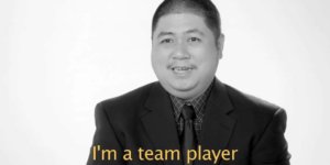 A man with a disability wearing a suit and tie speaking to camera in front of a white background. Caption: I'm a team player