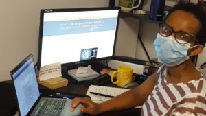 A black woman with a disability wearing a mask seated at a desk