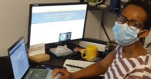 A black woman with a disability wearing a mask seated at a desk