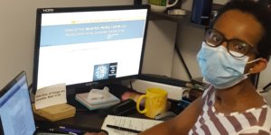 A black woman with a disability wearing a mask seated at a desk