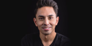 Danny Gomez smiling headshot wearing a black shirt in front of a black backdrop