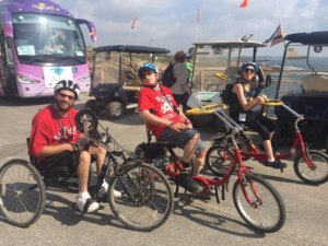 Blair Webb and two other participants on the birthright trip riding accessible bicycles in front of a large body of water