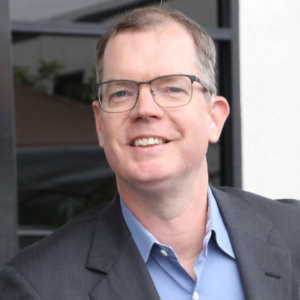 Headshot of Delbert Whetter wearing a blue collared shirt and gray blazer