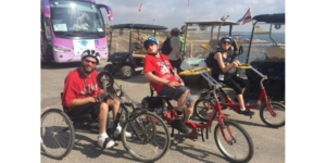 Blair Webb and two other participants on the birthright trip riding accessible bicycles in front of a large body of water