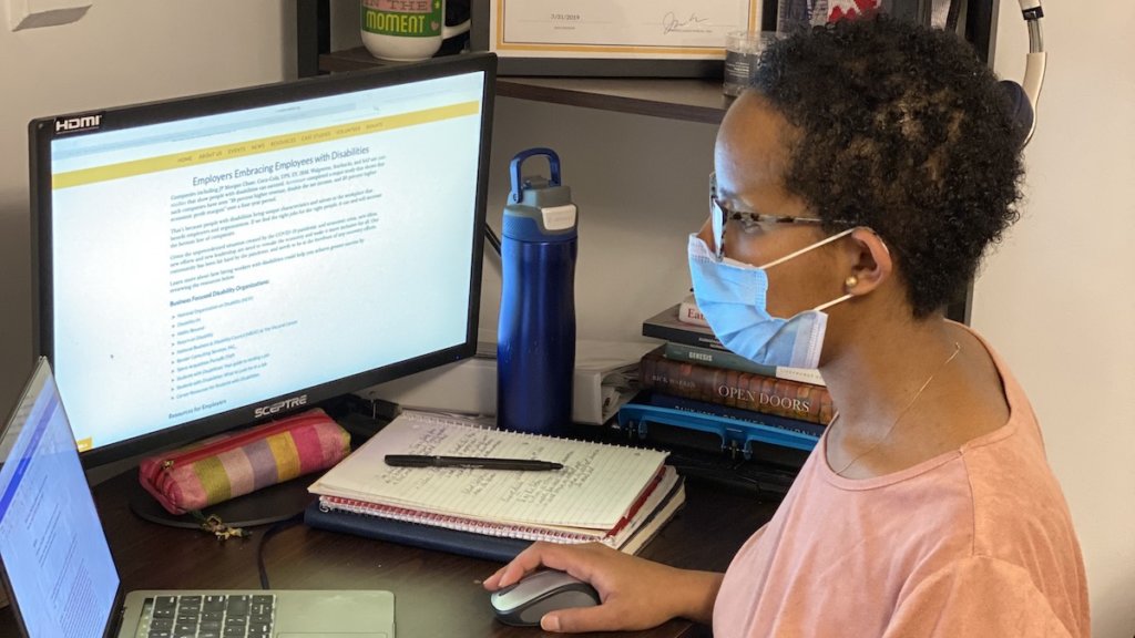 A black woman wearing a mask working on a computer