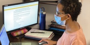 A black woman wearing a mask working on a computer