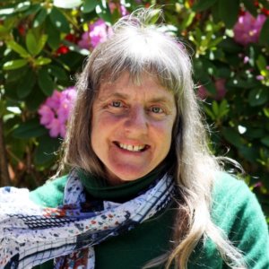 Susan Sygall smiling in front of bushes and flowers