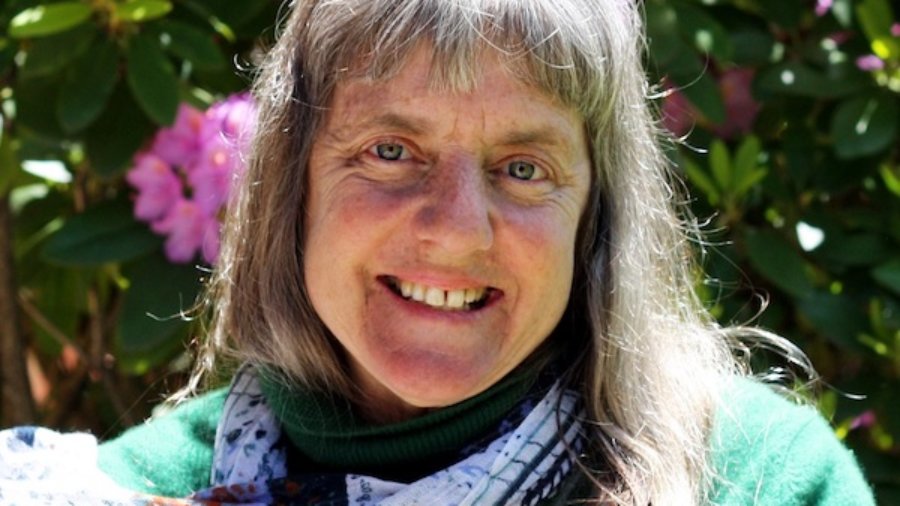 Susan Sygall smiling in front of bushes and flowers