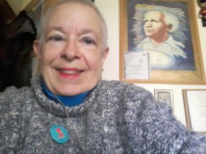 Carol Gould smiling in front of a painting of Israeli Prime Minister Ben Gurion