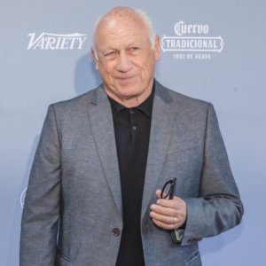 Joey Travolta wearing a suit smiling in front of a banner with the Variety logo on it