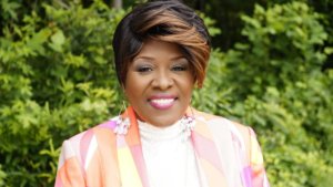 Norma Stanley smiling headshot wearing a colorful suit and standing in front of trees