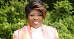 Norma Stanley smiling headshot wearing a colorful suit and standing in front of trees