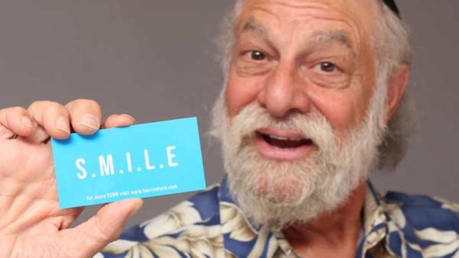 Barry Shore smiling holding up his business card with the word SMILE on it.