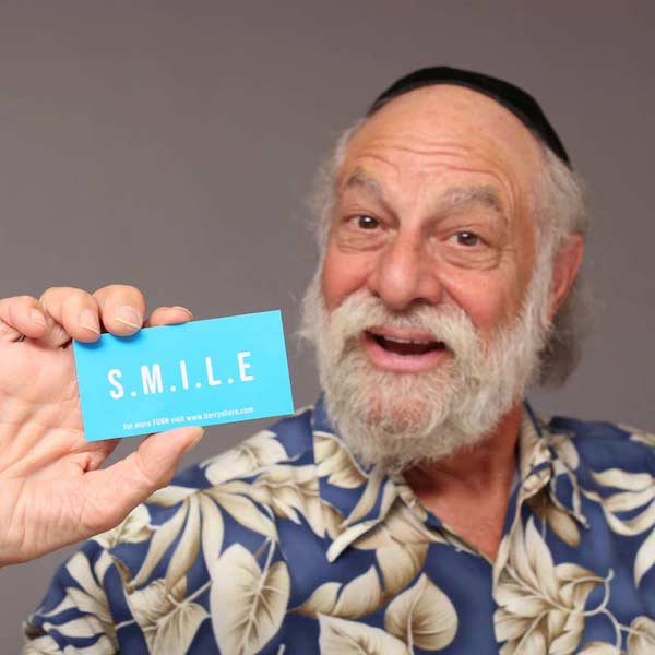 Barry Shore smiling holding up his business card with the word SMILE on it.