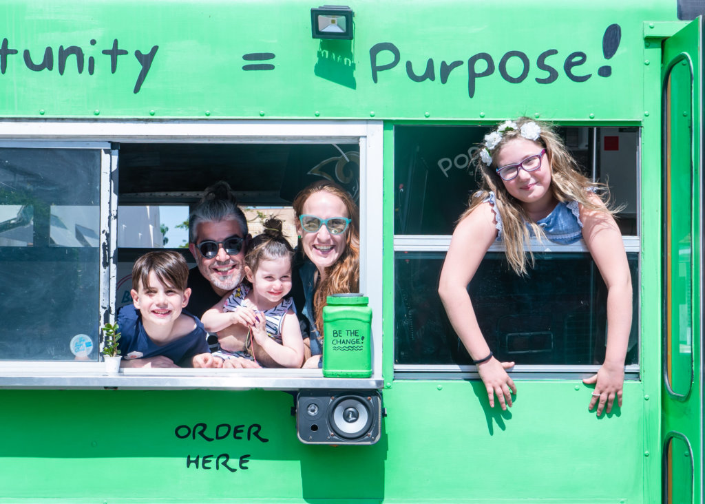 the Chernotsky family looking out the windows in a green bus, smiling