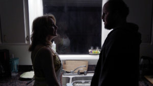 Eileen Grubba and Austin Basis talking with each other in a dark kitchen in a scene from Dead End Drive