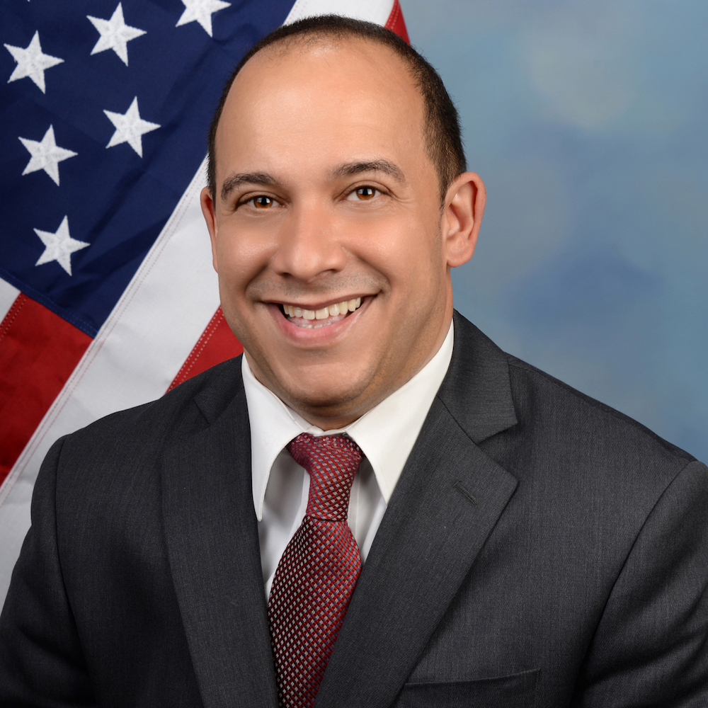 Joseph Bensmihen headshot smiling in front of an American flag