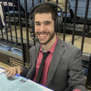 Justin Borses smiling wearing a headset and suit and tie while covering a game