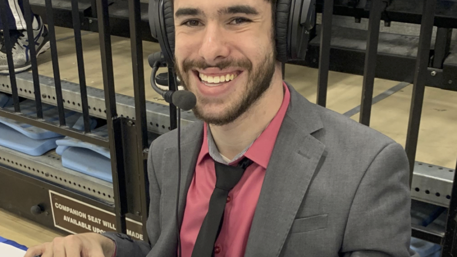 Justin Borses smiling wearing a headset and suit and tie while covering a game