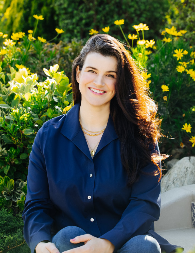 Leah Romond smiling headshot in front of yellow flowers and bushes