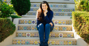 Leah Romond seated on a staircase, smiling. Photo by Liz Bretz