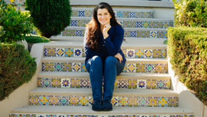 Leah Romond seated on a staircase, smiling. Photo by Liz Bretz