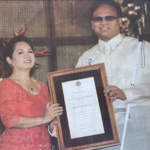 Ollie Cantos, dressed in Barong Tagalog, formal Filipino attire worn only on special occasions, accepting the Pride of the Filipino Award as presented by now-former Philippine President Gloria Macapagal-Arroyo at Malacañan Palace. Ollie’s Baromg is white with fabric made from pineapple fibers. President Arroyo is wearing a red dress.