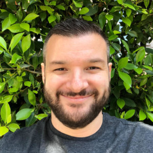 Shea Mirzai smiling headshot in front of green plants