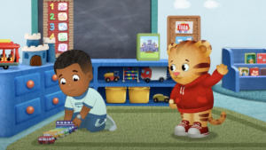 A scene from Daniel Tiger's Neighborhood with Max playing with toy trains and Daniel Tiger waving to him.