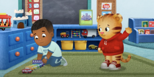 A scene from Daniel Tiger's Neighborhood with Max playing with toy trains and Daniel Tiger waving to him.