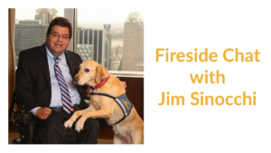 Jim Sinocchi sitting with a service dog in front of a window with skyscrapers behind him. Text: Fireside Chat with Jim Sinocchi