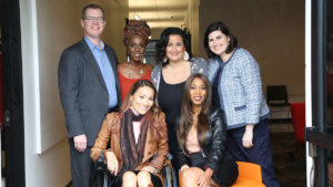 Six diverse people with disabilities smiling together inside a hallway