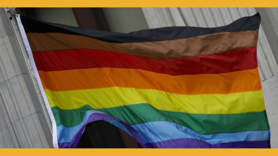 an LGBTQ+ Pride flag with black, brown, red, orange, yellow, green, blue and purple stripes