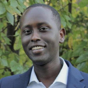 Headshot of Ian Cherutich smiling in front of trees and bushes.