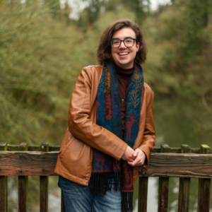 Leo Allanach smiling leaning against a wooden fence over a lake