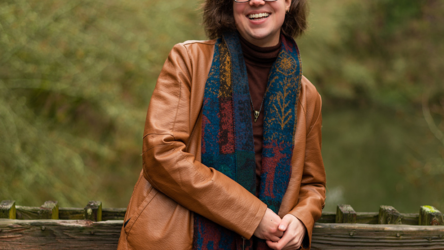 Leo Allanach smiling leaning against a wooden fence over a lake