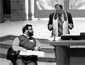 Matan Koch in a synagogue next to a rabbi with the Bimah brought down to the bottom of the staircase