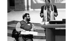 Matan Koch in a synagogue next to a rabbi with the podium brought down to the bottom of the staircase